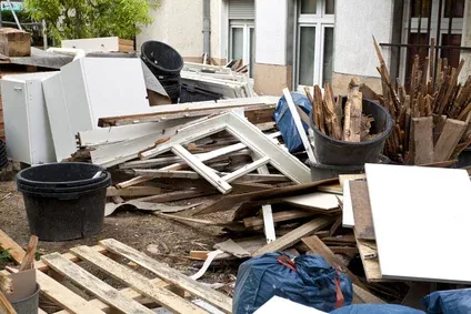 Aufgetürmter Sperrmüll vor einem Wohnhaus: alter Schrank, Holzbretter, Eimer und Bauschutt auf dem Hof